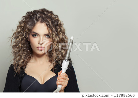 Glamorous young woman holding using hot curling tongs iron on white background. Glamorous young woman holding using hot curling tongs iron on white background. 117992566