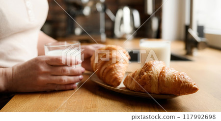 Girl with milk and croissants for breakfast Girl with milk and croissants for breakfast 117992698