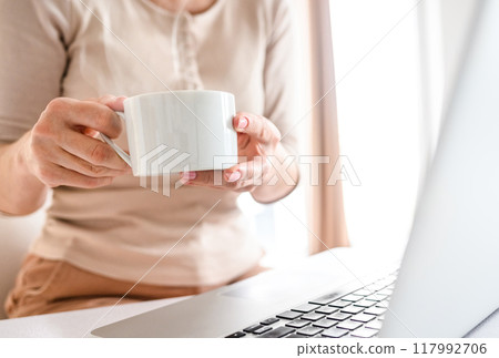 Girl drinking fresh morning coffee at the kitchen and using laptop 117992706