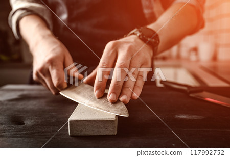 Man sharpening a knife with whetstone 117992752