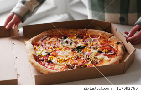 Girl Opened Cardboard Box With Fresh Delicious Meat And Vegetable Pizza 117992769