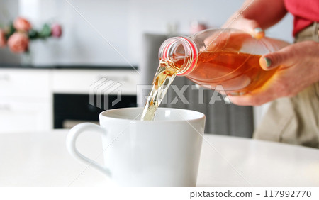 Girl Pouring Apple Juice Into Glass In The Kitchen, In Slow Motion 117992770