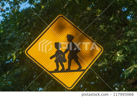 Yellow road sign with silhouettes of pedestrian children marked on it, signaling that there is a school nearby and there is a danger of children suddenly running out onto the roadway Yellow road sign with silhouettes of pedestrian children marked on it, signaling that there is a school nearby and there is a danger of children suddenly running out onto the roadway 117993066