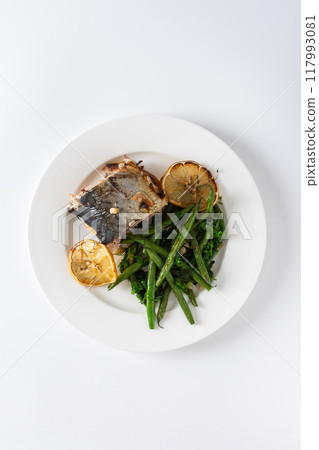 This savory dish features baked green beans with onions and tender mackerel, served on a plate against a white background, offering a healthy and balanced gourmet meal 117993081