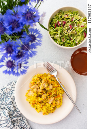 Stewed rice with chicken breast and mixed salad with radishes and various seeds, a served table with food and a vase of flowers Stewed rice with chicken breast and mixed salad with radishes and various seeds, a served table with food and a vase of flowers 117993167