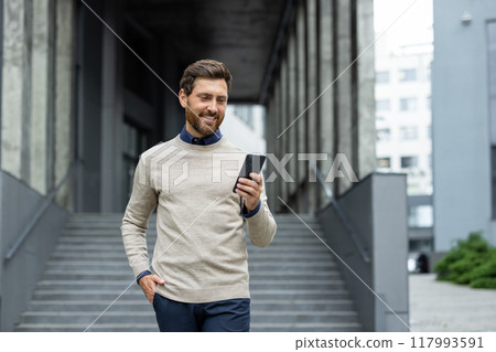 Smiling businessman walking outdoors using phone in urban area. Confident male professional engaging smartphone, reflecting modern lifestyle, communication, and technology in business environment Smiling businessman walking outdoors using phone in urban area. Confident male professional engaging smartphone, reflecting modern lifestyle, communication, and technology in business environment 117993591