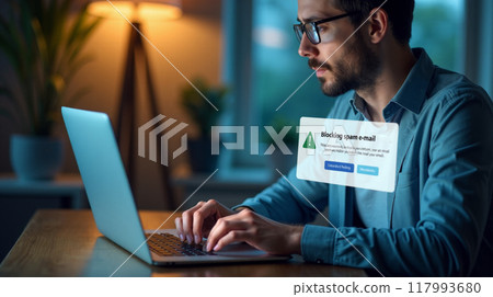 Man using laptop with spam blocking notification, internet security alert, email filtering action, cyber safety measure, home office setting, digital communication 117993680