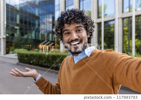 Cheerful businessman taking selfie outdoors, expressing happiness and confidence. Standing near modern office building with inviting smile and relaxed demeanor. Cheerful businessman taking selfie outdoors, expressing happiness and confidence. Standing near modern office building with inviting smile and relaxed demeanor. 117993783