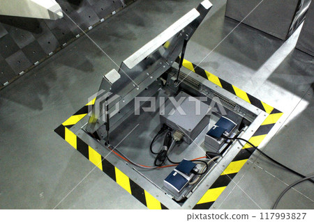 An open metal floor hatch revealing a panel of electrical components and wiring, providing access to essential industrial infrastructure 117993827