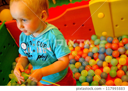 Little boy in a blue suit sitting in a box with colorful balls. Little boy in a blue suit sitting in a box with colorful balls. 117993883