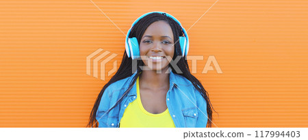 Happy African young woman listening to music with headphones, modern black teenage girl smiles 117994403