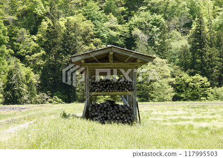 A landscape of a rural mountain area with fresh greenery, fields, and a rice rack hut 117995503