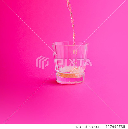 Sparkling drink being poured into glass on pink background 117996786