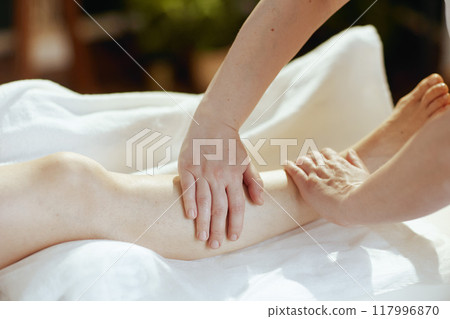 Medical massage therapist in spa salon massaging clients leg 117996870