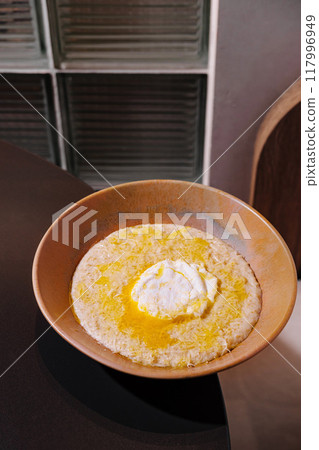 Bowl of creamy polenta with butter and cheese being served in restaurant setting 117996949