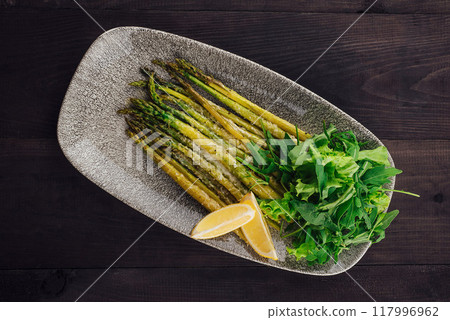 Roasted asparagus with lemon and arugula salad on a plate 117996962
