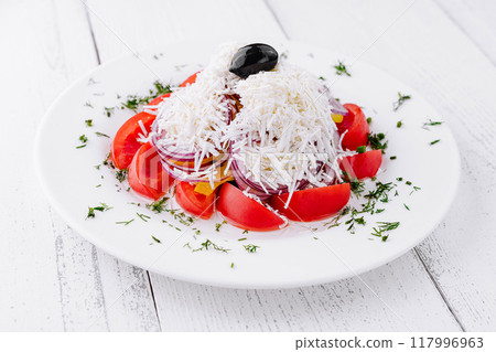 Shopska salad with tomatoes, onion, cheese, and olive sitting on white table 117996963