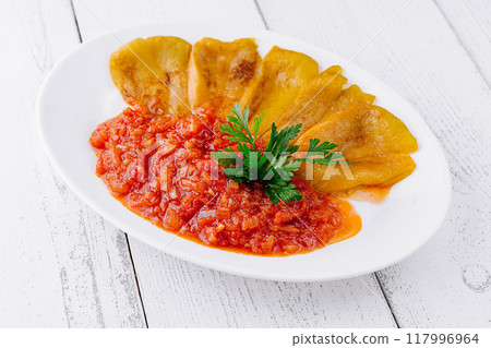 Delicious roasted yellow peppers lying on tomato sauce on white plate 117996964
