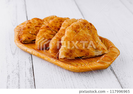 Delicious chebureki pastries resting on a wooden plate Delicious chebureki pastries resting on a wooden plate 117996965
