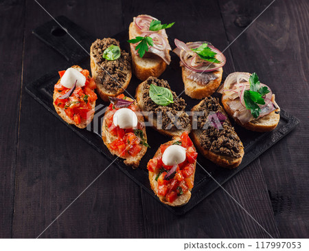 Different tasty bruschetta lying on black stone cutting board on wooden table 117997053