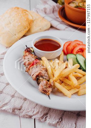 Grilled pork skewer with french fries and tomato sauce served on a plate 117997155