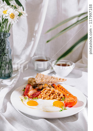 Full english breakfast with fried eggs, sausages, and beans served on white tablecloth Full english breakfast with fried eggs, sausages, and beans served on white tablecloth 117997188