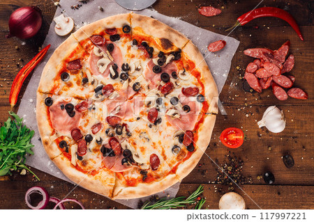 Delicious pizza lying on wooden table surrounded by fresh ingredients Delicious pizza lying on wooden table surrounded by fresh ingredients 117997221