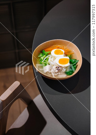 Steaming chicken noodle soup with eggs on restaurant table 117997315