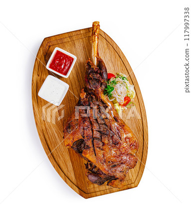 Roasted lamb shank with vegetables and sauces on wooden board 117997338