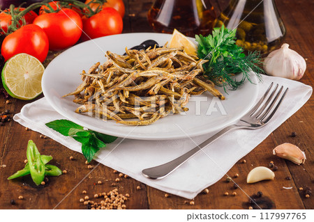 Fried anchovies served on white plate with herbs and spices on rustic wooden table 117997765