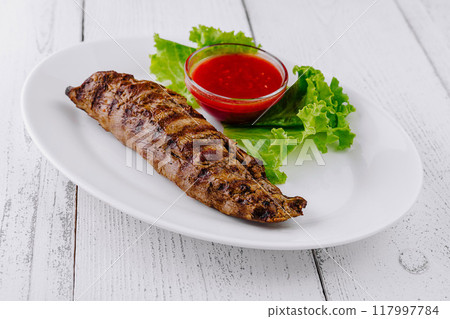 Delicious grilled steak lying on white plate with lettuce and red sauce 117997784