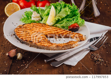 Grilled salmon steak with lettuce and lemon on white plate Grilled salmon steak with lettuce and lemon on white plate 117997853