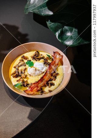 Creamy polenta with mushrooms and poached egg served in restaurant 117997937