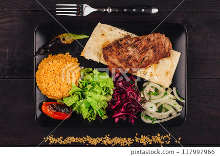 Grilled meat dish served on black plate with vegetables and bulgur Grilled meat dish served on black plate with vegetables and bulgur 117997966