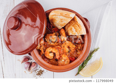 Aromatic seafood stew with shrimps is served in clay pot on white wooden table Aromatic seafood stew with shrimps is served in clay pot on white wooden table 117998049