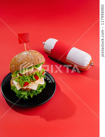 Delicious double burger standing on black plate with sausage on red background 117998060