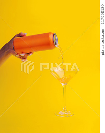 Woman pouring orange drink from can into glass with yellow background Woman pouring orange drink from can into glass with yellow background 117998120