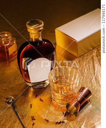 Bottle of liquor with blank label and a glass of alcohol on gold background Bottle of liquor with blank label and a glass of alcohol on gold background 117998171