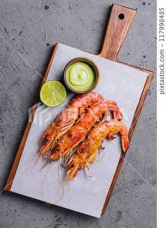 Grilled prawns on wooden board with lime and sauce 117998485