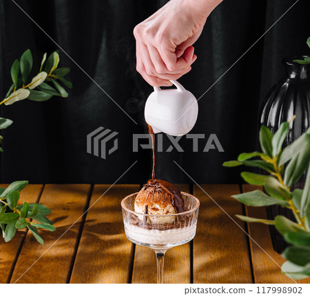 Hand pouring sauce over ice cream close up 117998902