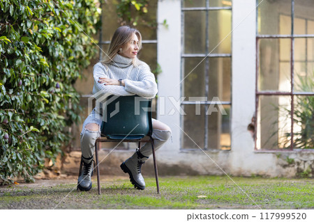 Young woman wearing casual clothes posing sitting on a chair in a garden 117999520
