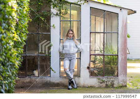 Young woman posing leaning on the wall of an old greenhouse Young woman posing leaning on the wall of an old greenhouse 117999547