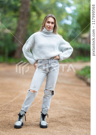 Attractive young woman posing in the park wearing jeans and sweater Attractive young woman posing in the park wearing jeans and sweater 117999568