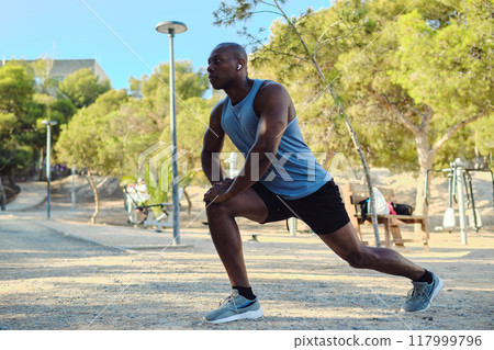 African athletic man do leg stretching exercises outdoors 117999796