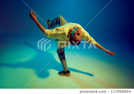 Flexible man in casual clothes, catching energetic then and performing hip-hop dance against gradient blue background in neon light Flexible man in casual clothes, catching energetic then and performing hip-hop dance against gradient blue background in neon light 117999844