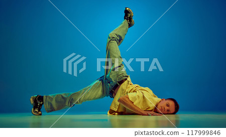 Flexible man in casual clothes, catching energetic then and performing hip-hop dance against gradient blue background in neon light 117999846