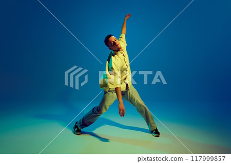 Lost in the music. Dynamic image for young man, hip-hop dancer making energetic performance against gradient blue background in neon light Lost in the music. Dynamic image for young man, hip-hop dancer making energetic performance against gradient blue background in neon light 117999857