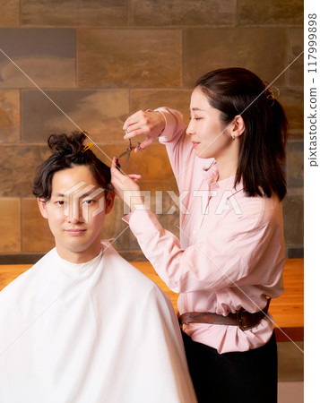 A female hairdresser cutting a hair and a male customer, hair salon, beauty salon image 117999898
