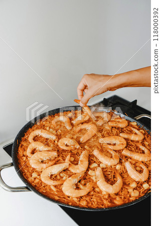 man ads some shrimps to the fideua, a noodle paella 118000392