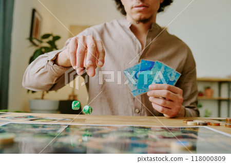 Unrecognizable young man holding cards throwing dice while playing modern fantasy board game 118000809